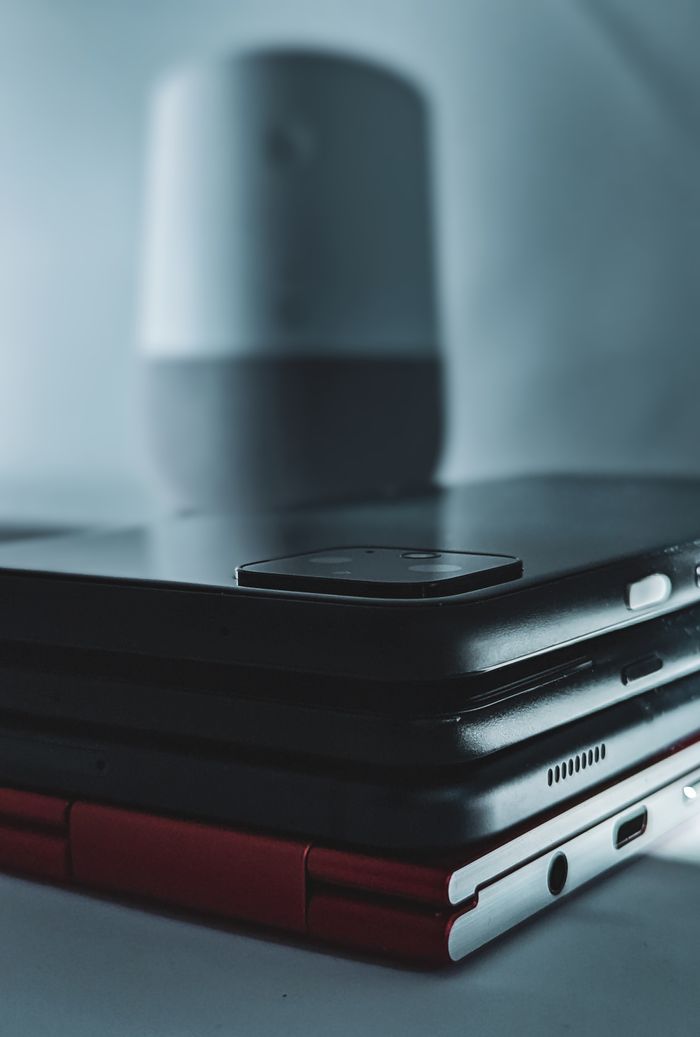 Close-up of stacked modern devices including smartphones and a tablet with wireless speaker in background.